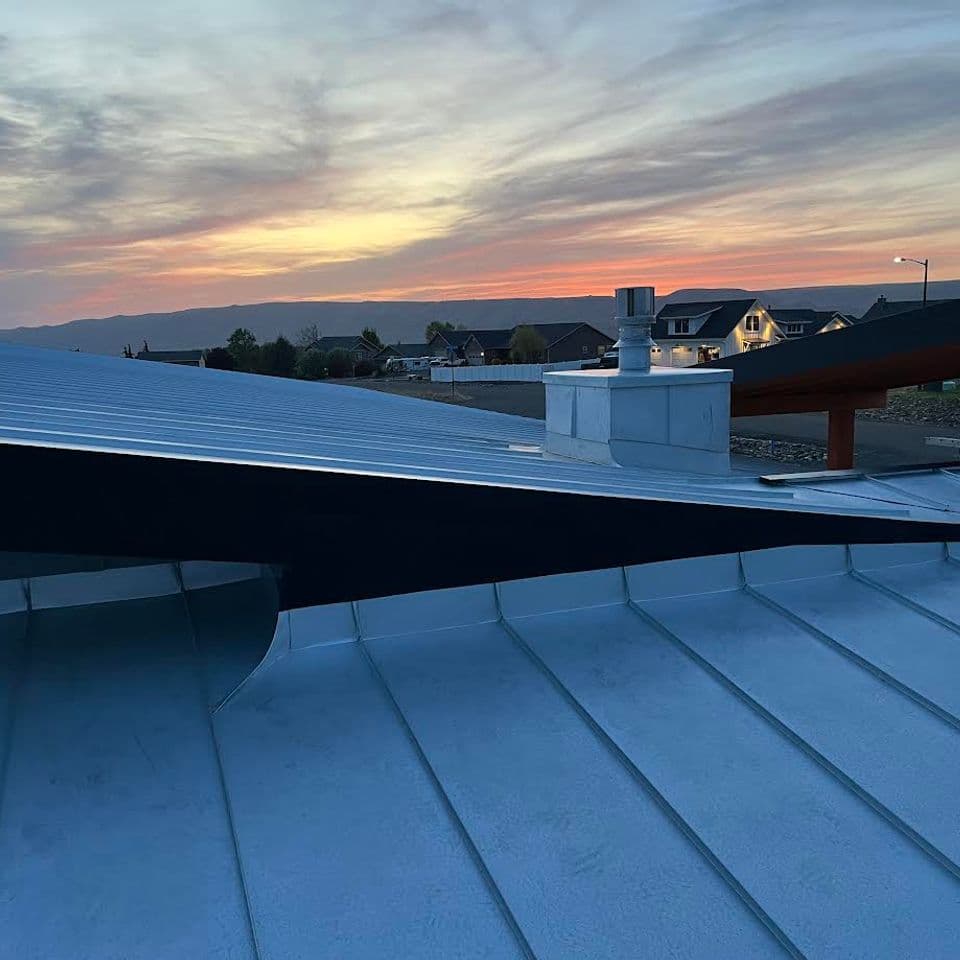 Metal roof at sunset with colorful sky and houses in the background, showcasing modern architecture.