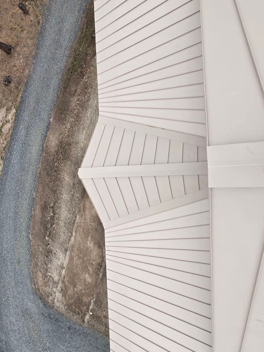 Aerial view of a metal roof with sharp angles, alongside a gravel pathway.