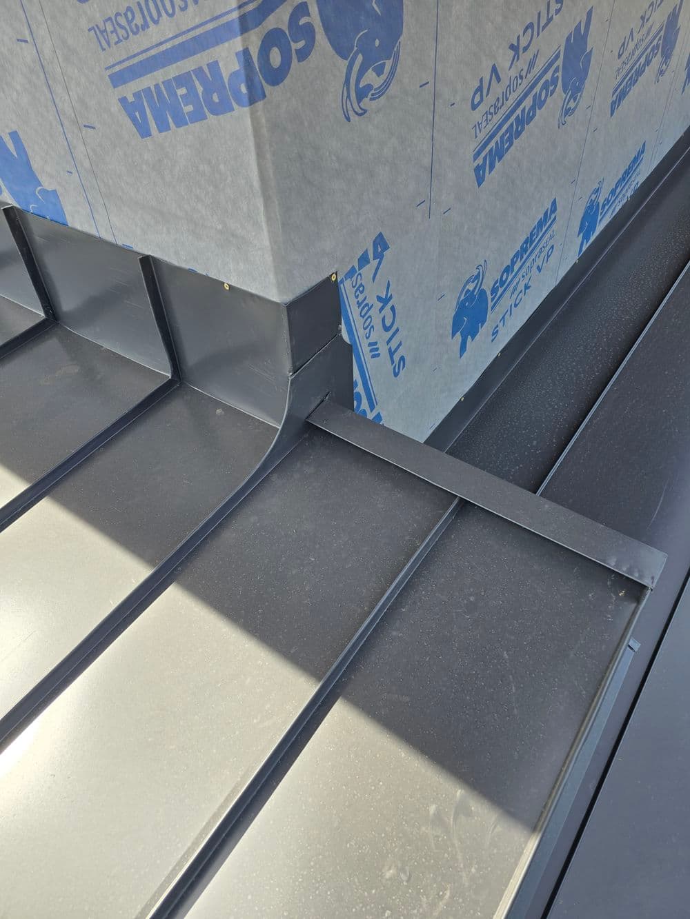 Metal roof installation detail with flashing and underlayment visible in sunlight.