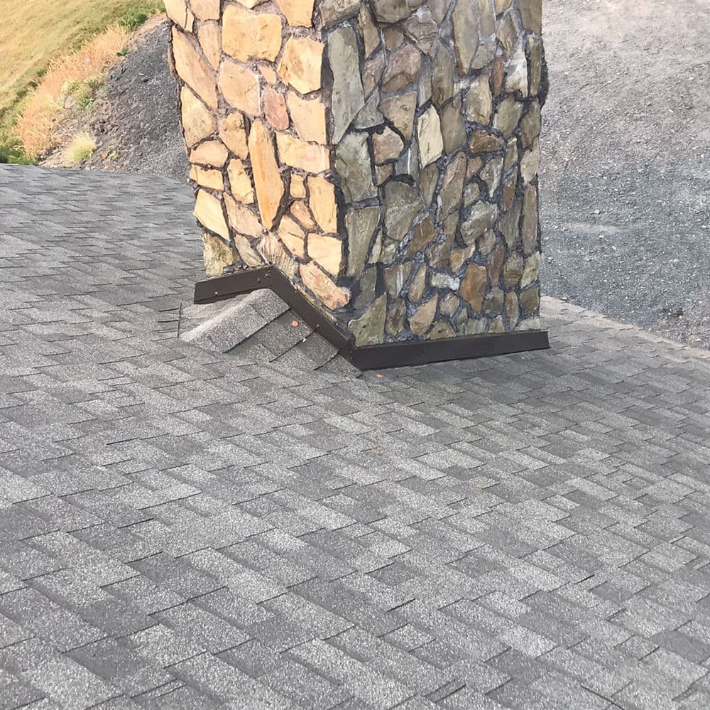 Stone pillar on a rooftop with asphalt shingles and metal flashing detail.
