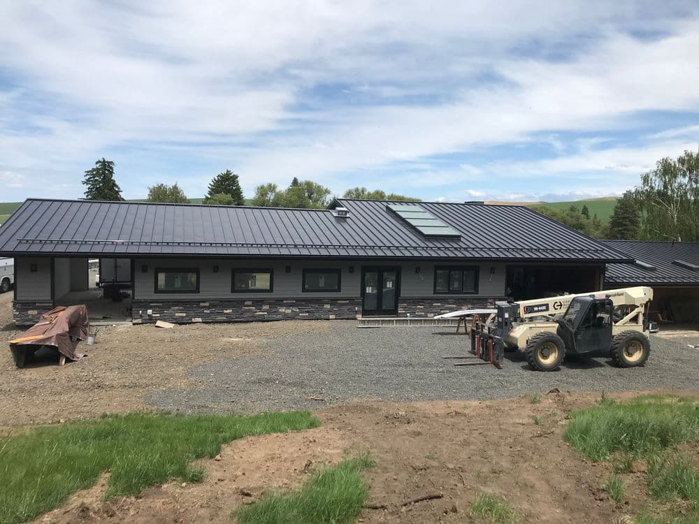 Modern one-story home under construction with a sleek metal roof and stone accents.